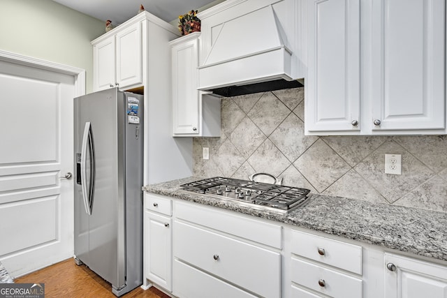 kitchen featuring custom range hood, light stone countertops, stainless steel appliances, white cabinetry, and backsplash