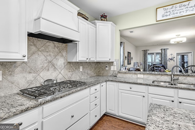 kitchen featuring tasteful backsplash, stainless steel gas cooktop, custom range hood, white cabinetry, and a sink