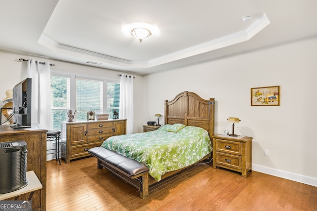 bedroom featuring light wood-style floors, visible vents, a tray ceiling, and ornamental molding