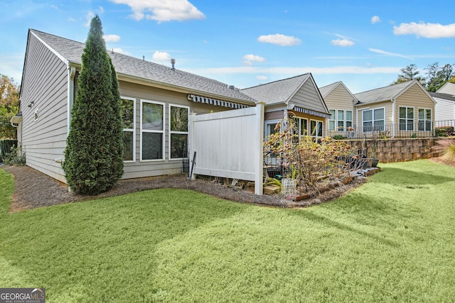 rear view of house with fence, a lawn, and roof with shingles