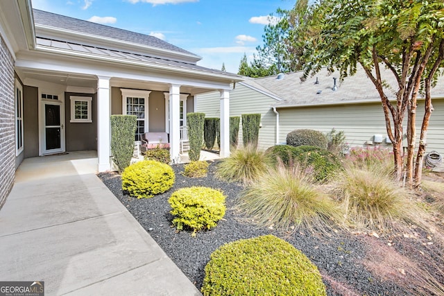 entrance to property with covered porch and a shingled roof