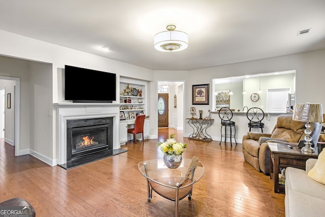 living area featuring baseboards, visible vents, built in features, hardwood / wood-style flooring, and a fireplace