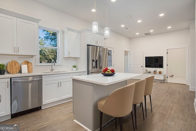 kitchen with stainless steel appliances, white cabinets, sink, pendant lighting, and light wood-type flooring