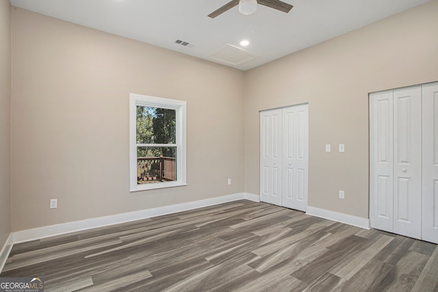 unfurnished bedroom featuring ceiling fan, dark hardwood / wood-style floors, and multiple closets