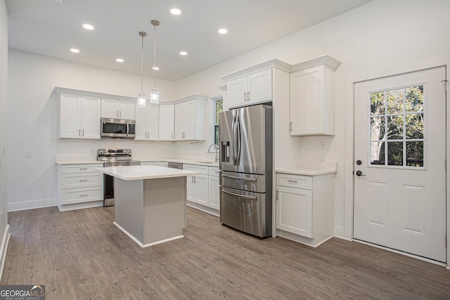 kitchen featuring sink, appliances with stainless steel finishes, hanging light fixtures, a kitchen island, and white cabinets