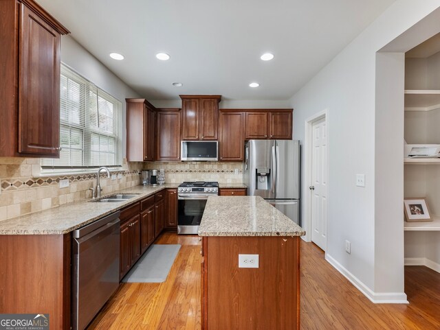 kitchen with appliances with stainless steel finishes, sink, a kitchen island, light stone counters, and light hardwood / wood-style flooring