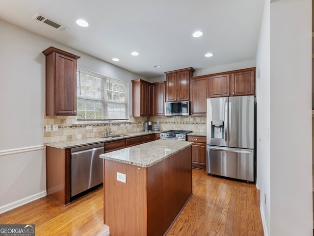 kitchen featuring a kitchen island, stainless steel appliances, sink, light stone countertops, and light wood-type flooring