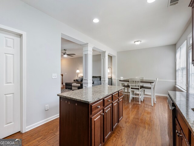 kitchen featuring ceiling fan, a kitchen island, light stone countertops, hardwood / wood-style flooring, and ornate columns