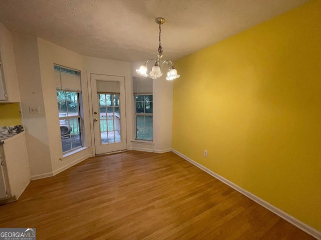 unfurnished dining area featuring light wood-type flooring, a textured ceiling, baseboards, and an inviting chandelier