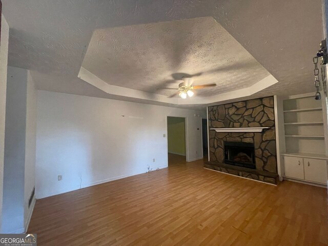 unfurnished living room with a tray ceiling, wood finished floors, baseboards, a textured ceiling, and ceiling fan