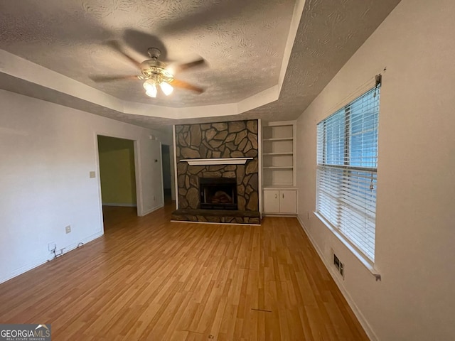 unfurnished living room with built in features, a raised ceiling, visible vents, light wood-style floors, and a textured ceiling