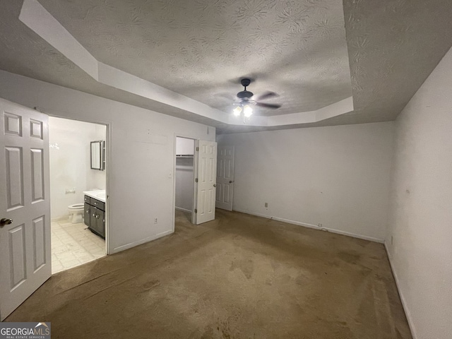 unfurnished bedroom with light carpet, a textured ceiling, a raised ceiling, baseboards, and a walk in closet