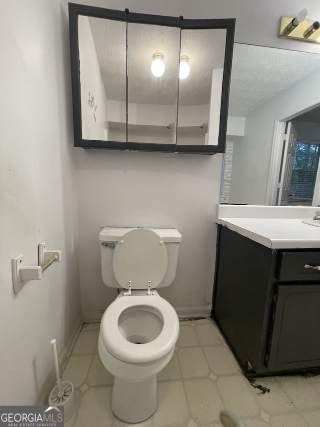 bathroom featuring a textured ceiling, toilet, vanity, baseboards, and tile patterned floors