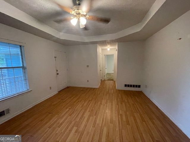 empty room featuring a raised ceiling, wood finished floors, a ceiling fan, and visible vents
