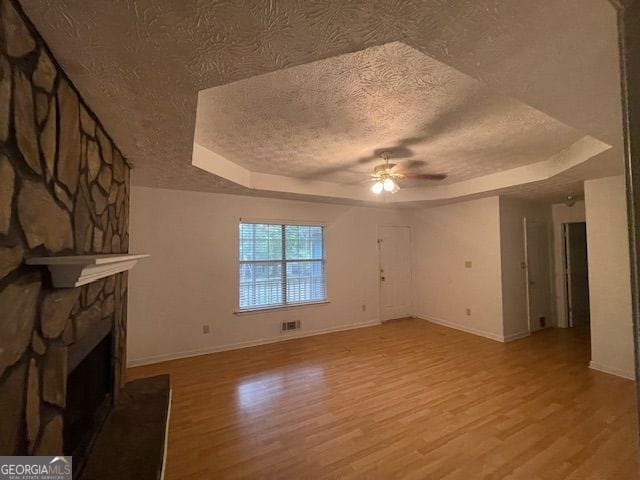 unfurnished living room featuring light wood-type flooring, a raised ceiling, a fireplace, and a textured ceiling