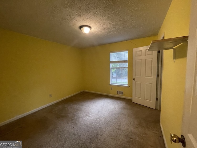 spare room with a textured ceiling and dark colored carpet