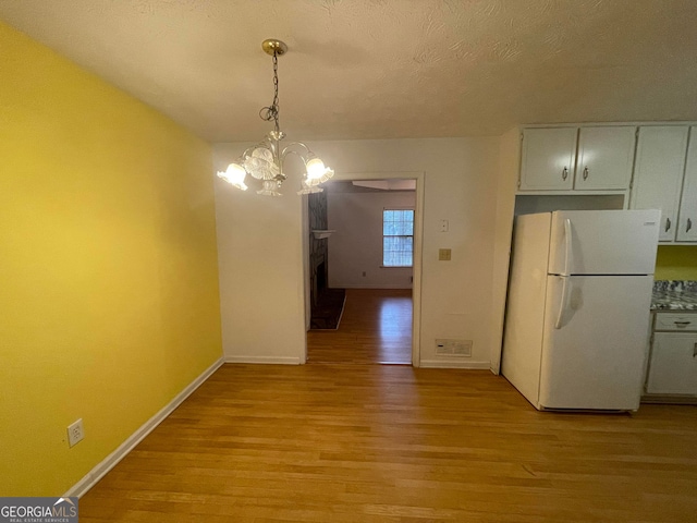 unfurnished dining area featuring baseboards, a textured ceiling, light wood-type flooring, a fireplace, and a chandelier