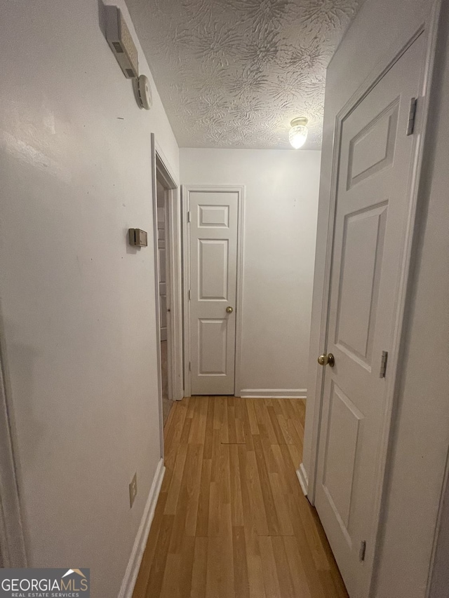 hallway featuring a textured ceiling, light wood-style flooring, and baseboards