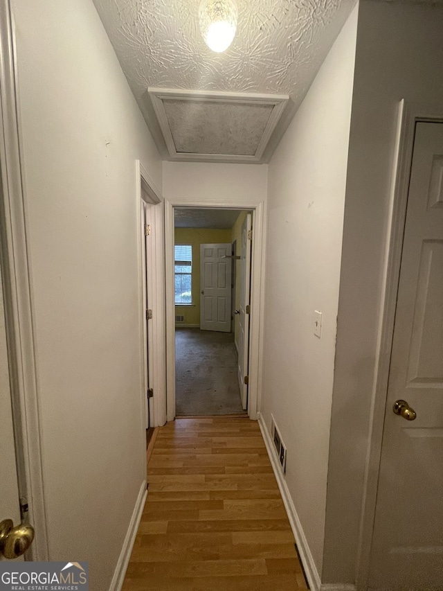 hall featuring visible vents, attic access, a textured ceiling, wood finished floors, and baseboards