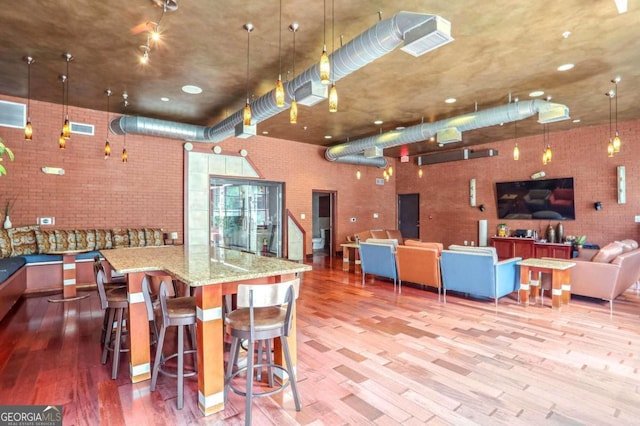 kitchen with a large island, a kitchen breakfast bar, light stone countertops, wood-type flooring, and decorative light fixtures