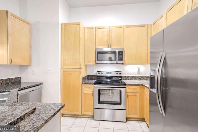 kitchen featuring light brown cabinets, appliances with stainless steel finishes, dark stone counters, and light tile patterned floors