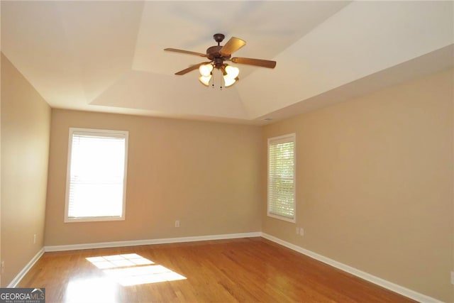 empty room with ceiling fan, light hardwood / wood-style floors, and a raised ceiling