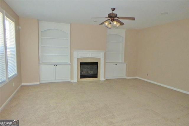 unfurnished living room featuring ceiling fan, built in shelves, and light colored carpet