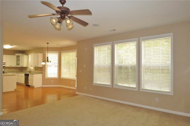 unfurnished living room featuring light colored carpet, sink, and ceiling fan with notable chandelier