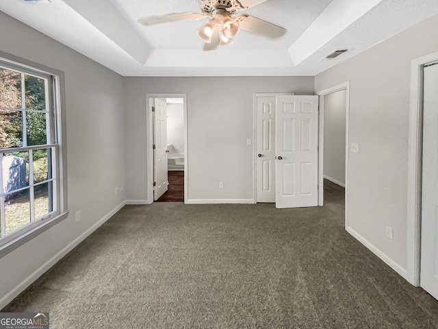 unfurnished bedroom with ceiling fan, a raised ceiling, and multiple windows