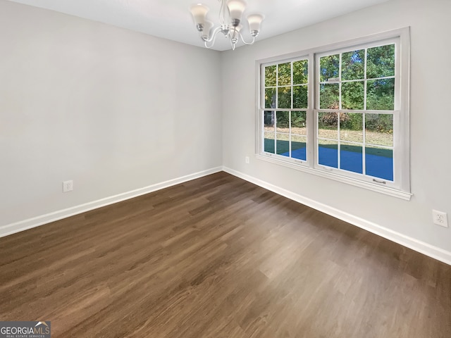 empty room featuring dark wood-type flooring and a chandelier