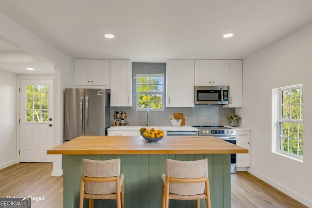 kitchen with appliances with stainless steel finishes, light wood-type flooring, white cabinets, and plenty of natural light