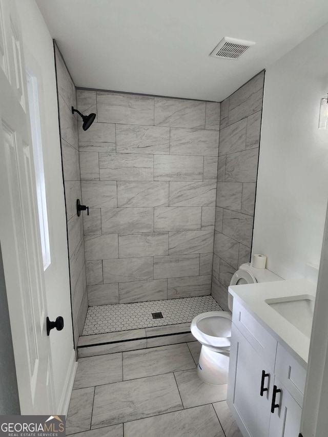 bathroom with vanity, tiled shower, and toilet