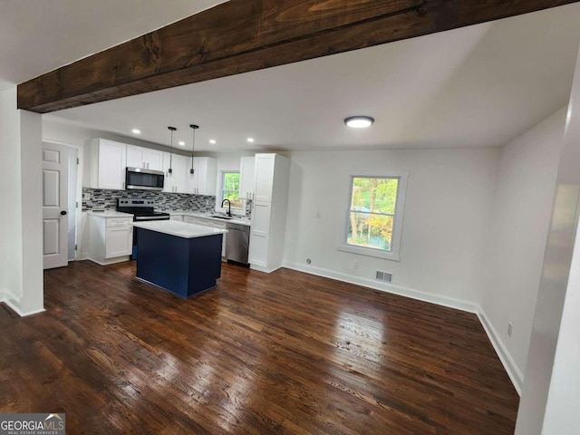 kitchen featuring white cabinets, beam ceiling, dark hardwood / wood-style flooring, appliances with stainless steel finishes, and a kitchen island