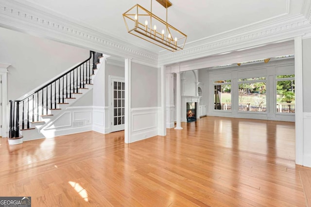 unfurnished living room with ornamental molding, an inviting chandelier, and hardwood / wood-style floors