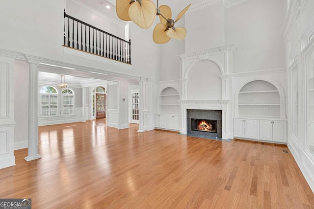 unfurnished living room with light hardwood / wood-style flooring, built in features, and a high ceiling