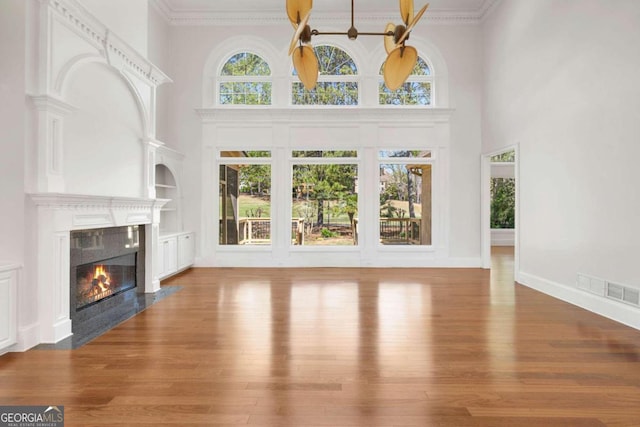 unfurnished living room with a wealth of natural light, a high end fireplace, wood-type flooring, and built in features