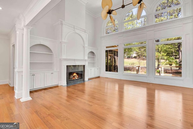 unfurnished living room with a high ceiling, ornate columns, light hardwood / wood-style flooring, built in shelves, and ceiling fan