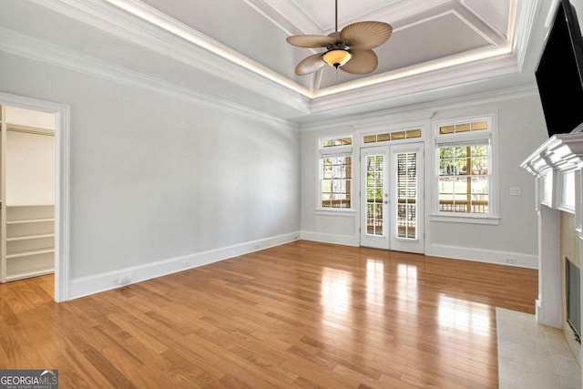 unfurnished living room featuring french doors, ornamental molding, light wood-type flooring, a raised ceiling, and ceiling fan