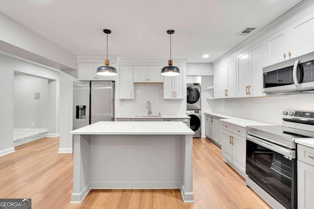 kitchen with stacked washer / dryer, appliances with stainless steel finishes, light wood-type flooring, and white cabinetry