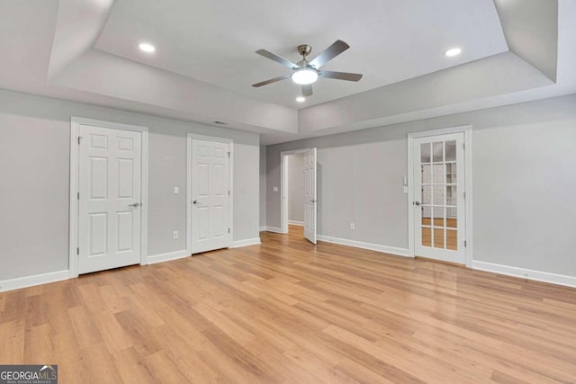 unfurnished bedroom featuring ceiling fan, a raised ceiling, and light hardwood / wood-style flooring