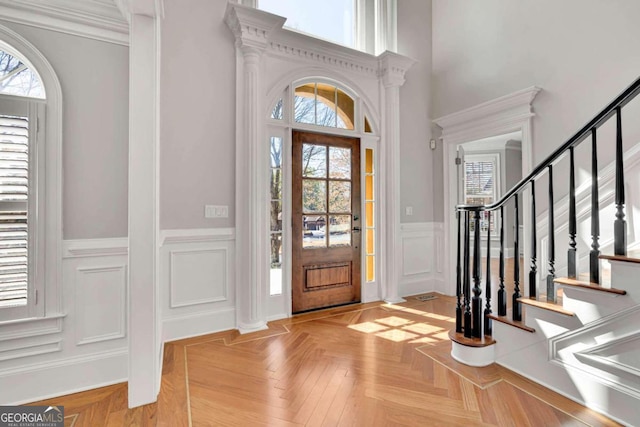 entrance foyer with ornate columns, crown molding, and light parquet flooring