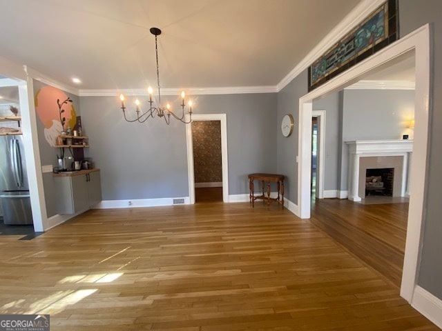 unfurnished dining area featuring ornamental molding, an inviting chandelier, and hardwood / wood-style floors