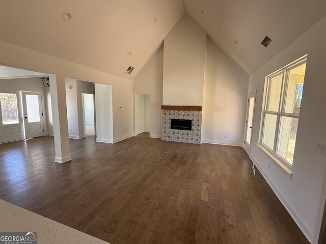 unfurnished living room with high vaulted ceiling, dark wood-type flooring, and a tile fireplace