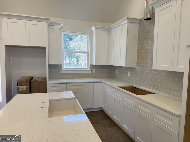 kitchen featuring white cabinetry, lofted ceiling, sink, decorative backsplash, and light stone countertops