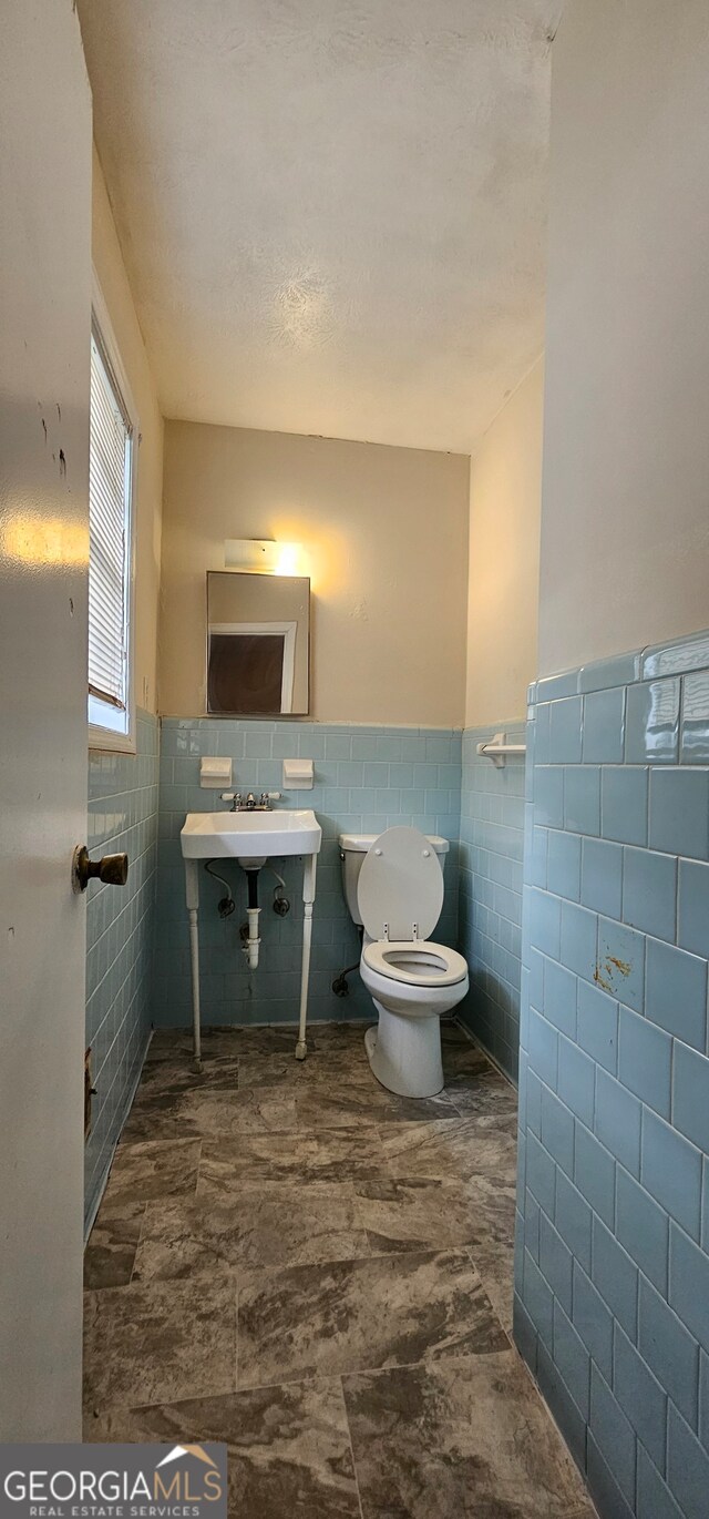 bathroom featuring toilet, sink, and tile walls