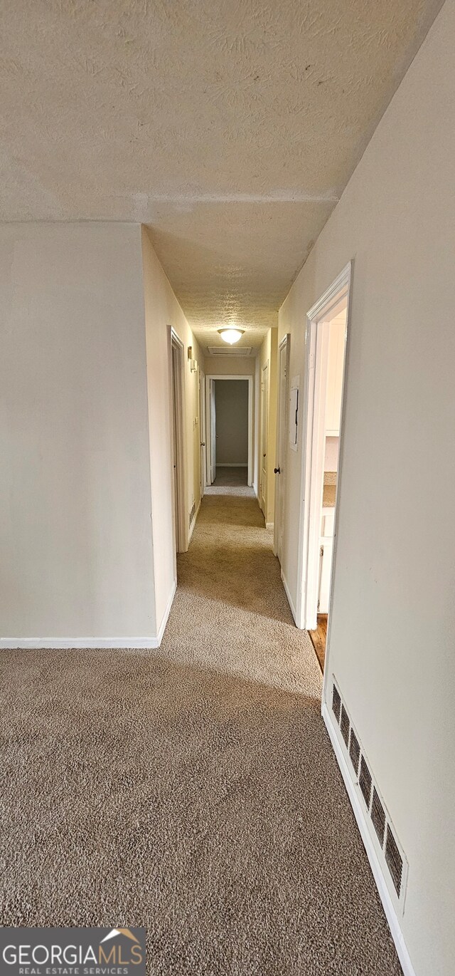 hall with light carpet and a textured ceiling