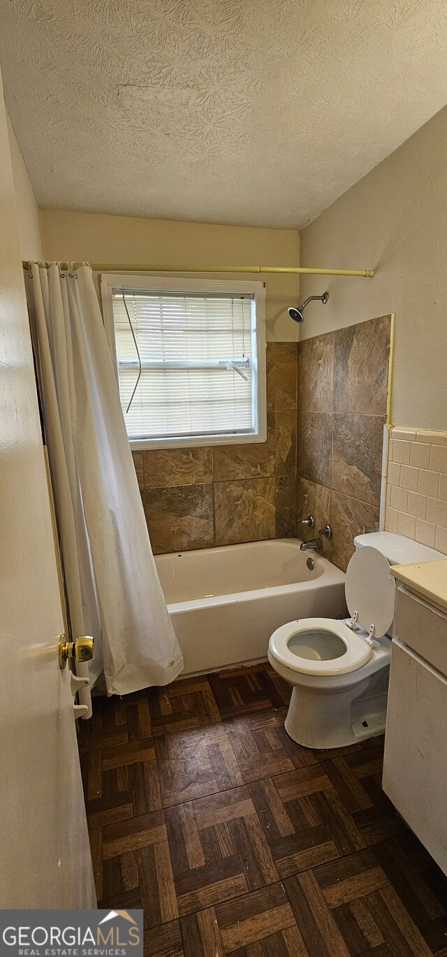 full bathroom featuring shower / bath combo, toilet, vanity, tile walls, and a textured ceiling