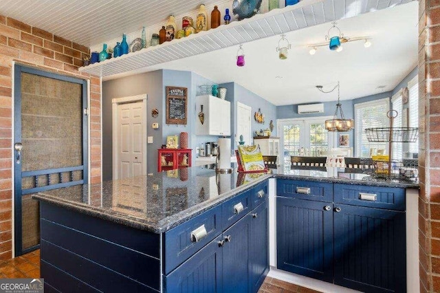 kitchen with dark stone counters, pendant lighting, a wall unit AC, blue cabinetry, and brick wall