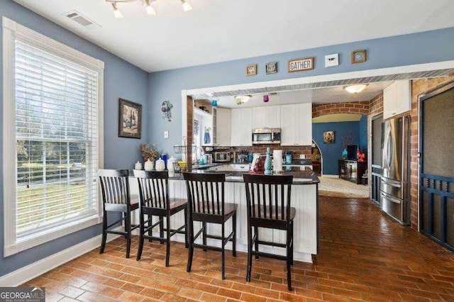 kitchen with a kitchen bar, appliances with stainless steel finishes, white cabinetry, and kitchen peninsula