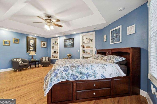 bedroom with a raised ceiling, light hardwood / wood-style floors, and ceiling fan